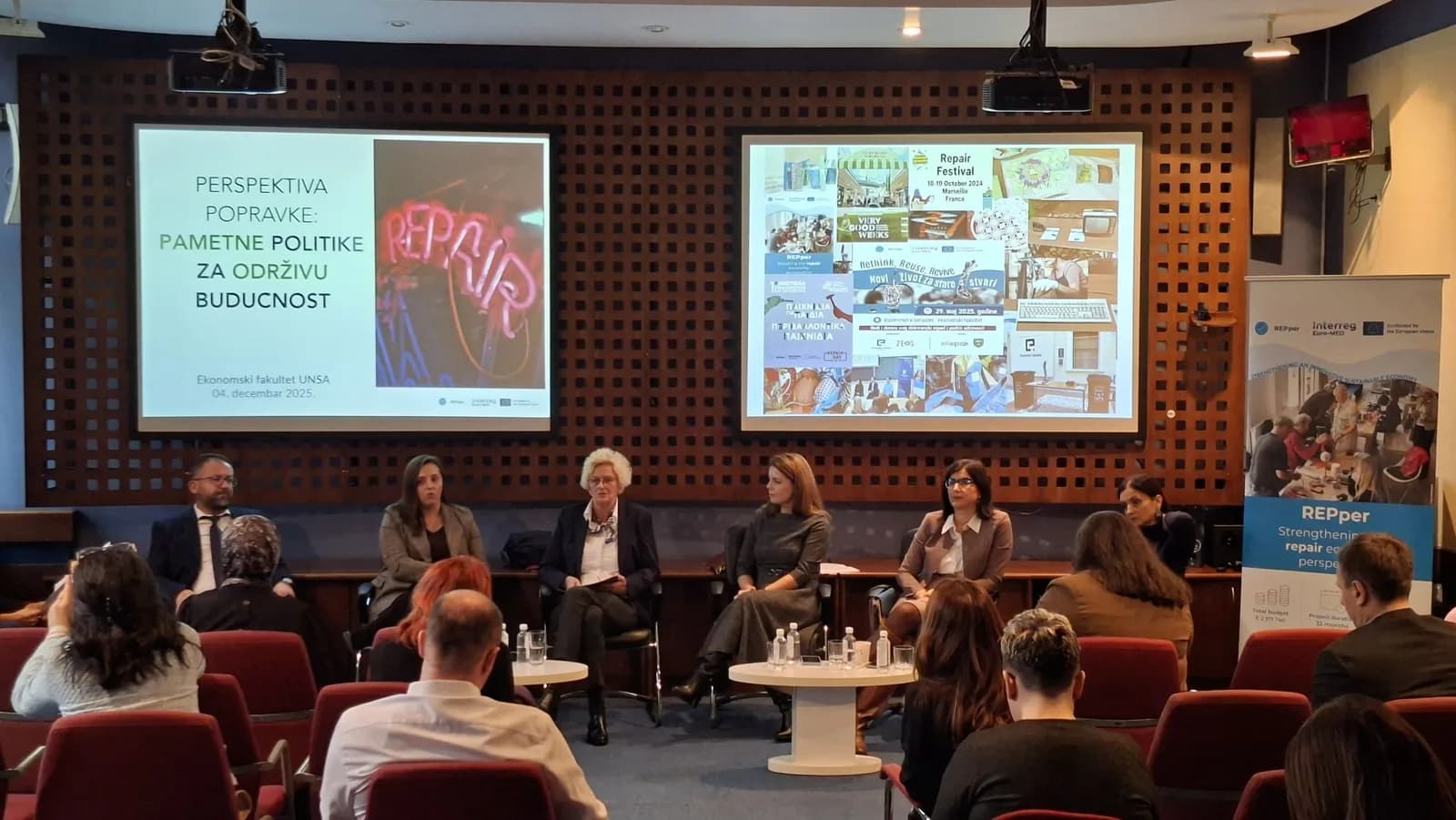 Panelisti i publika na okruglom stolu „Perspektiva popravke: Pametne politike za održivu budućnost“, uz prezentacije i REPper baner.